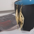Elegant golden alloy leaf and feather tassel drop earrings on a ceramic mug edge - Gold