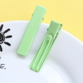 Close-up of mint green macaron hair clips on a white ceramic plate with a yellow background - Matte Matcha Green
