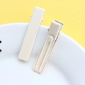 Close-up of two cream-colored metal alligator hair clips on a decorative plate - Matte Off-white
