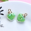 Detailed view of a heart-shaped glass pendant filled with green star sequins and gold clasp - 1.8 x 2.4cm / Grass Green
