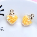 Detail view of heart-shaped glass pendants filled with yellow star sequins and silver rings - 1.8 x 2.4cm / Yellow