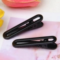 Close-up of sleek black U-shaped hair clips with glossy finish on a floral background - Black
