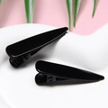 Close-up of black non-slip hair clips with glossy finish on a minimalist ceramic base - Black