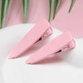 Close-up of pink macaron hair clips on a white ceramic plate with green palm leaves - Pink