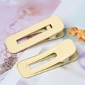 Detail of two cream yellow square duckbill hair clips with a glossy finish and hollow design - Off White