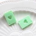 Vue macro de breloques poker en résine vert clair avec cœur évidé sur plateau blanc - Vert fruit