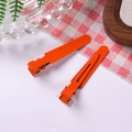 Close-up of matte orange metal alligator hair clips for DIY crafts on a table - Orange Red