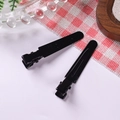 Close-up of dual glossy black metal alligator hair clips with reflective finish on fabric - Black
