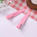 Detail of two pink metal duckbill hair clips on red checkered fabric and rustic background - Peach