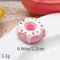 Close-up of pink resin donut miniature with white icing on a white wavy plate - Pink Base White Cream Colorful Dots