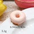 Macro detail of a 2.4cm resin donut charm with realistic pink glaze on a white porcelain plate - Pink