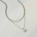Drielaagse zilveren kralenketting met een Cupido-munt hanger op witte getextureerde achtergrond - Staalkleur