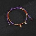 Detail of bohemian purple woven bracelet with gold sun charm and white pearl accent - Sun