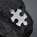 Detailed macro view of a polished stainless steel puzzle piece pendant on dark natural stone - Vertical Puzzle Pendant / Steel