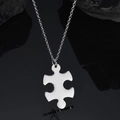 Polished silver jigsaw puzzle pendant necklace on a dark reflective surface - Vertical Puzzle Necklace / Steel