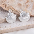 Polished silver shell charms for DIY jewelry making on a textured stone and seashell background - Polished Scallop
