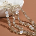 Strand of champagne faceted crystal rondelle beads draped over a white ceramic bowl - Transparent-Tea Brown