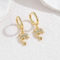 Close-up of golden dolphin hoop earrings with white zircon inlay on white marble - Dolphin