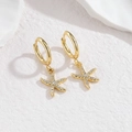 Macro shot of gold starfish earrings with sparkling zircon stones on a marble surface - Starfish