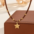 Macro view of a 18k gold star pendant on a brown cord with beaded accents - Textured Star Style (S-N2298-C)