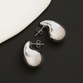 Primer plano de pendientes de gota en plata pulida sobre fondo minimalista texturizado - Pendientes de Gota de Agua Plateados