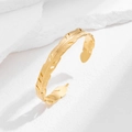 Close-up of golden adjustable hollow feather bangle on white textured stone display - Feather Style (1132) / Gold