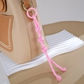 Detailed close-up of a pink hand-woven nylon rope knot charm attached to a beige leather bag - Button Knot Style / Pink
