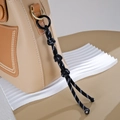 Detail of hand-woven black and white nylon cord charm attached to a leather bag - Button Knot Style / Black