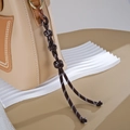 Close-up of leather handbag with braided knot charm and gold metal ring detail - Button Knot Style / Dark Coffee