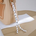 Detail of a black and white braided nylon cord charm attached to a khaki leather handbag - Button Knot Style / White