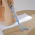 Detail von himmelblauem geflochtenem Taschenanhänger mit Knoten an khakifarbener Handtasche - Knopfknoten-Stil / Blau