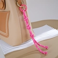 Nahaufnahme eines rosa handgewebten Nylon-Taschenanhängers an einer beige Ledertasche - Knopfknoten-Stil / Rosarot