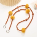 Detailed view of plush mobile phone strap with brown beads and yellow fur pom poms - Coffee