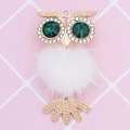 Detail view of owl keychain with white fur ball and green crystal eyes in gold metal - White