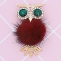 Detail of owl pendant featuring emerald crystal eyes and a plush burgundy fur body - Burgundy