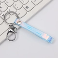 Iridescent light blue laser PU leather keychain with silver lobster clasp on a keyboard - Blue