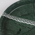 Detailaufnahme von weißem Spitzenband mit geometrischen Mustern auf dunkelgrünem Marmor - 07w15mma