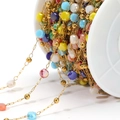 Golden bead chain with colorful crystal beads on white spool for DIY jewelry making - Colorful