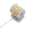 Detailed macro view of 7mm gold stainless steel chain with white shell beads on a spool - Off-white