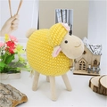 Detalle de oveja de peluche amarilla con flor rosa y campana sobre fondo de madera - Amarillo