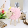 Peluche de oveja rosa con flor amarilla y cascabel sobre fondo de madera natural - Rosa