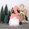 Pink glowing Christmas gnome with knitted hat and bell decoration in festive home setting - Pink