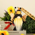 Close-up of bee gnome plush with striped hat, yellow beard, and wings in a garden setting - Yellow Striped Hat