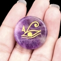 Natural purple amethyst stone with gold engraved Eye of Horus symbol shown in hand - Amethyst