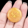 Pierre de cristal jaune plate avec gravure dorée de l'Œil d'Horus tenue en main - Jade Jaune