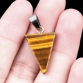 Polished tiger eye stone triangle pendant with silver metal clasp on hand model - Tiger's Eye