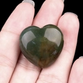 Polished natural green agate heart pendant with red patterns held in hand - India Agate