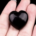 Handheld view of a heart-shaped black agate stone pendant with a polished smooth finish - Obsidian