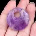 Runder violetter Amethyst Donut Anhänger mit Natursteintextur auf einer Hand - Amethyst