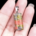 Hand holding a 20mm cylindrical natural crystal pendant with mixed multi-color texture - Unakite